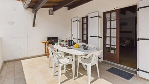 Eine Terrasse mit Tisch und Stühlen, eine Tür mit Glasscheiben und eine Holzbalkendecke.