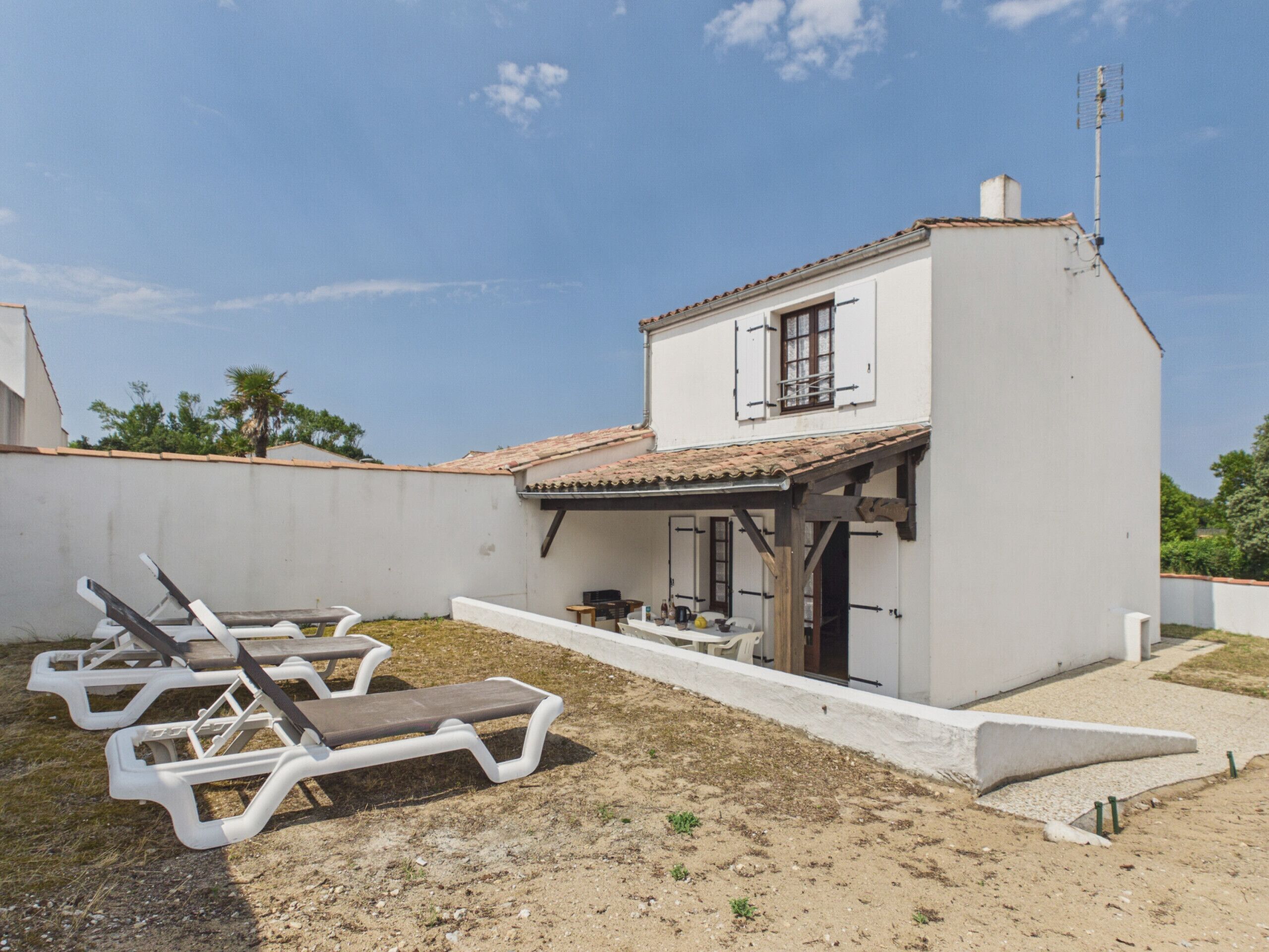 A white building with a tiled roof, a covered patio, and two lounge chairs.