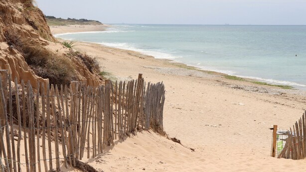 Ein sandiger Strand mit einer Holzumzäunung und freiem Blick auf den Ozean.