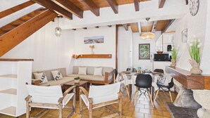 Ein gemütliches Interieur mit Holzbalkendecke, einer Couch, einem Esstisch, Stühlen und einer Küchenzeile.