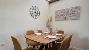 Een eetgedeelte met een houten tafel, vier stoelen, een wandklok en een schilderij.