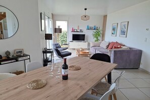 Ein modernes Wohnzimmer mit einem Holzesstisch, einer Couch, einem Fernseher und einem großen Fenster.
