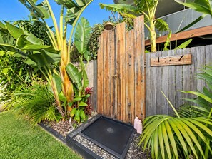 A garden with a wooden fence, a black planter box, and various tropical plants. - A Little Ocean Breeze - A charming coastal escape (Manyana)