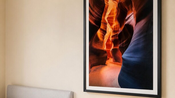 Un lit bien fait, avec des oreillers, une table de chevet sur laquelle se trouve une lampe, et un tableau représentant un canyon accroché au mur.