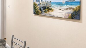 Un coin repas avec une table et des chaises, un tableau représentant une scène de plage accroché au mur, et une porte visible au fond.