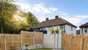 Un jardin avec une terrasse dallée, une pelouse, une clôture en bois et une maison avec un toit en tuiles.