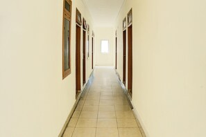 Un long couloir étroit, avec des portes en bois de chaque côté, qui mène à une grande fenêtre au bout.