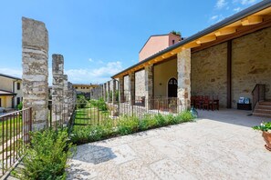 Un patio con ruinas de piedra, una zona de estar cubierta y un edificio de piedra con tejado de baldosas.