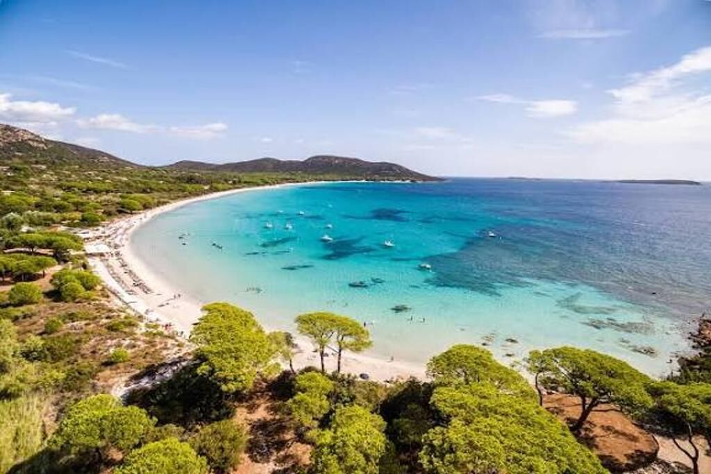 A coastal landscape with a beach, clear blue waters, and green vegetation.