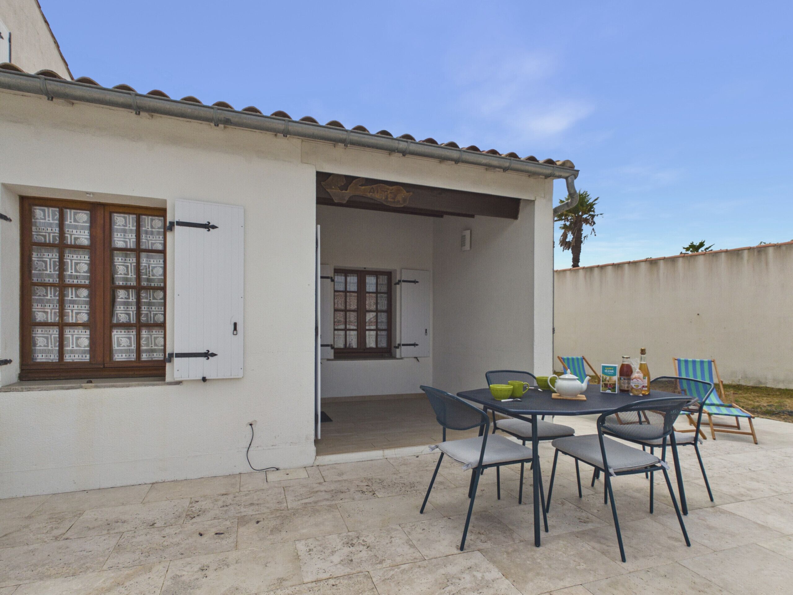 Eine Terrasse mit Tisch und Stühlen, einer Tür und einem Fenster mit Rollläden.