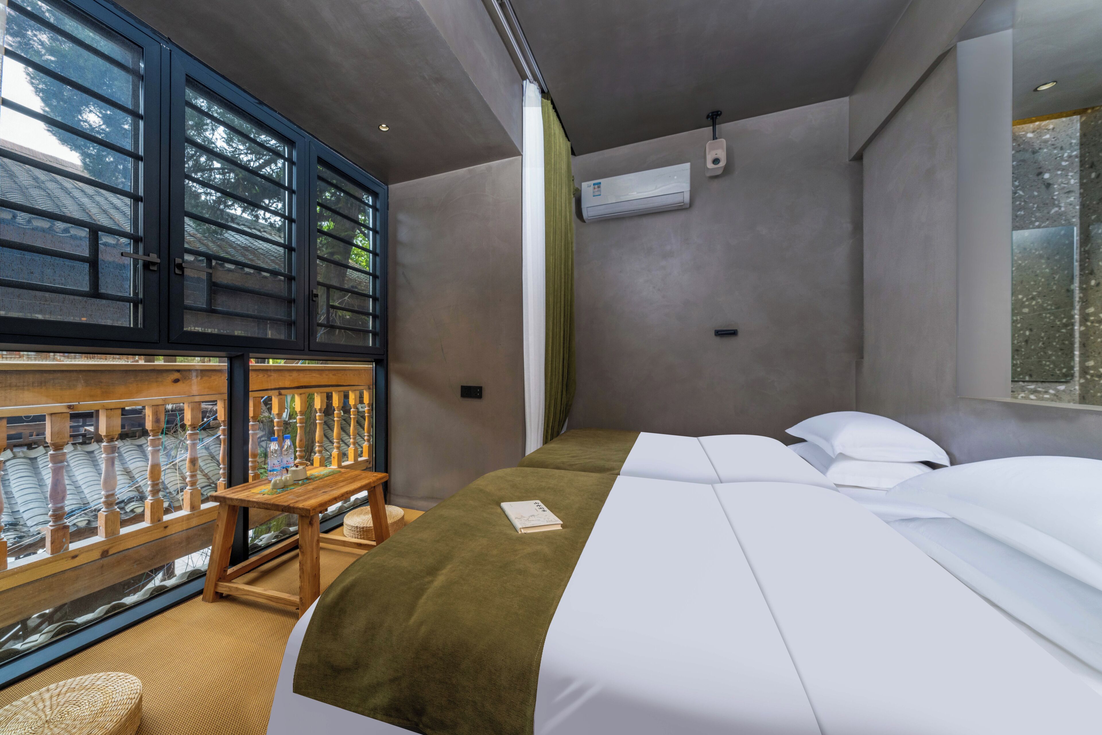 A room with a bed, a small table, a window with a view, and an air conditioning unit.