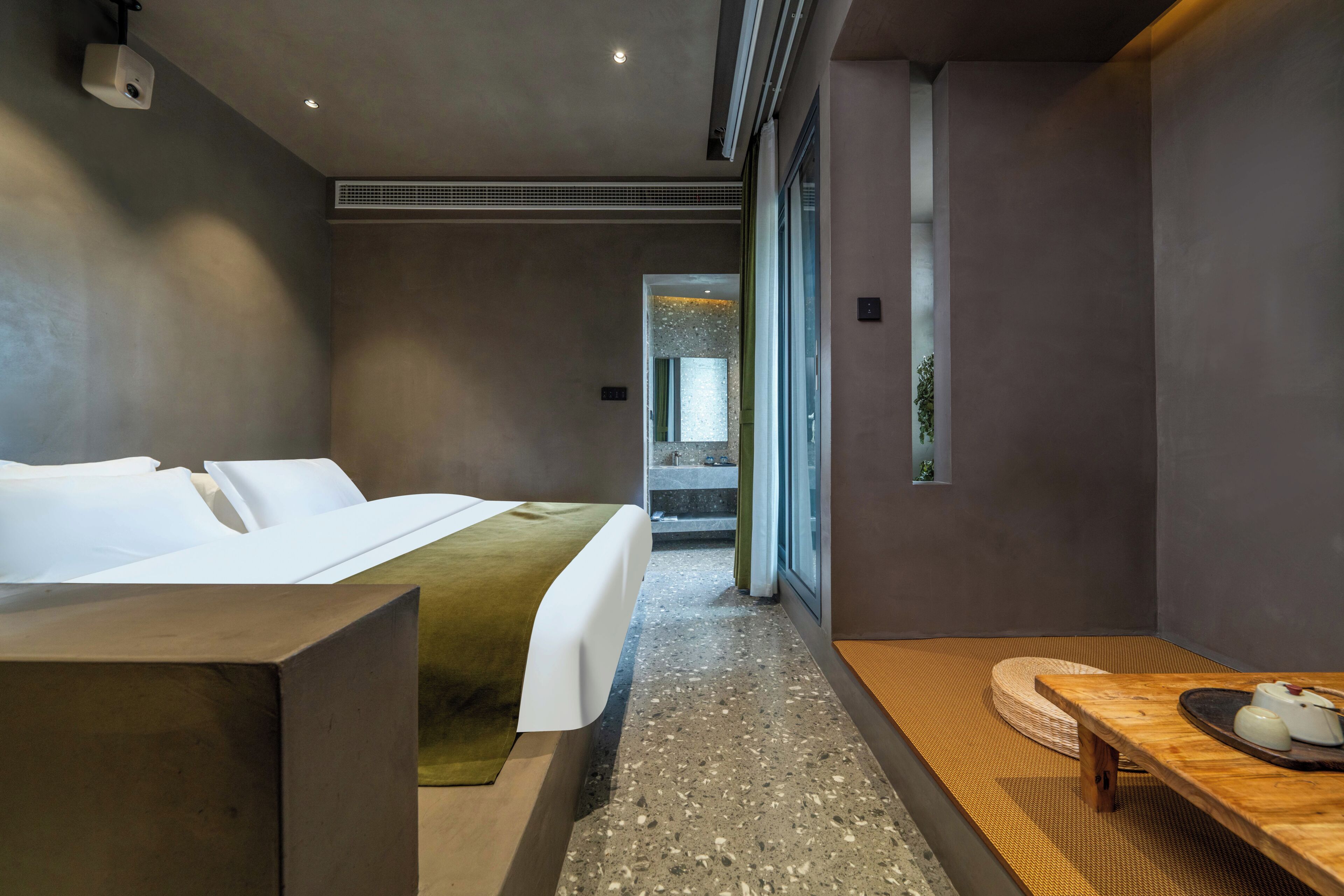 Une chambre d’hôtel moderne, dotée d’un lit, d’une table en bois et offrant une vue sur un jardin grâce à de grandes fenêtres.