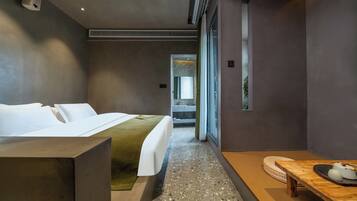 Une chambre d’hôtel moderne, dotée d’un lit, d’une table en bois et offrant une vue sur un jardin grâce à de grandes fenêtres.