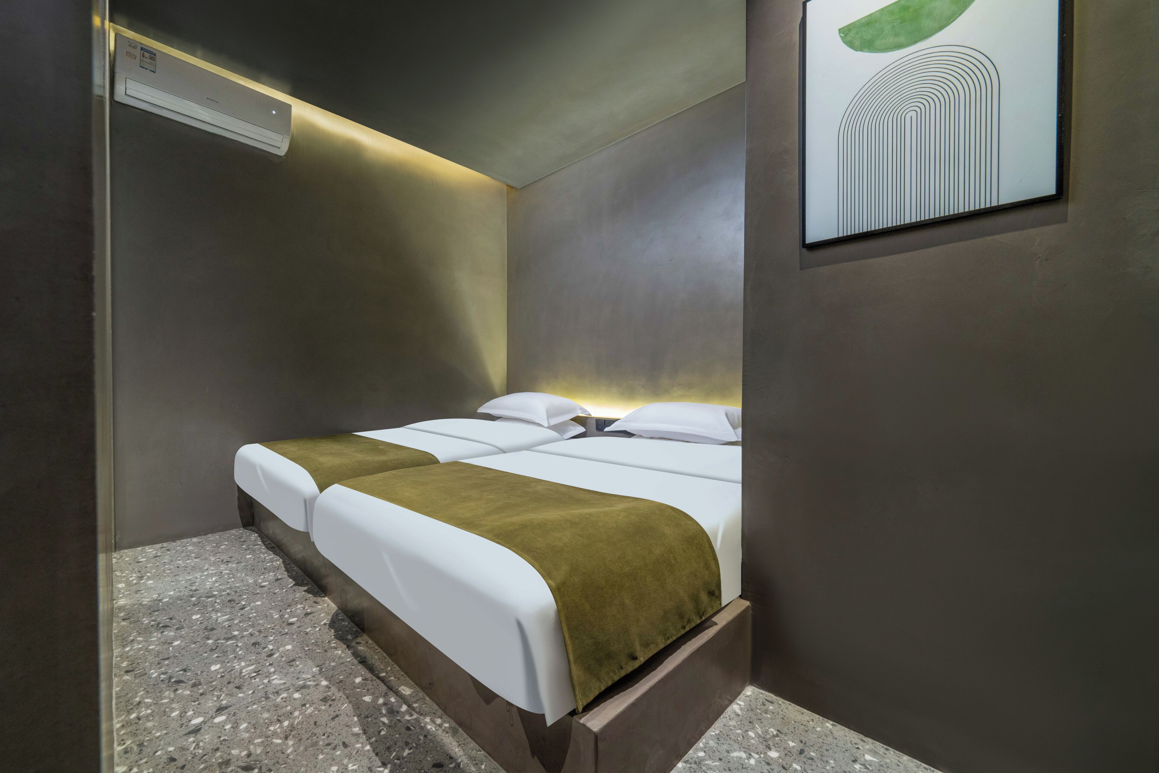 A hotel room with a bed, a wall-mounted air conditioner, and a framed abstract artwork.