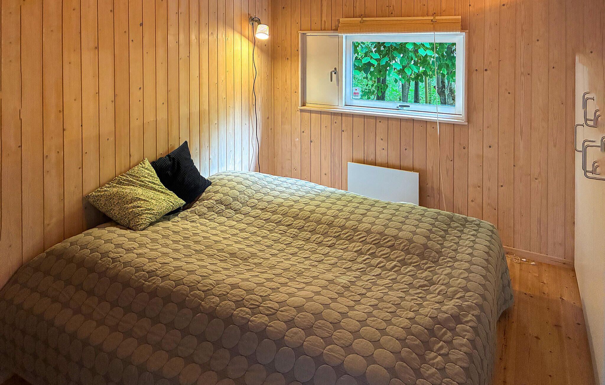 Ein Zimmer mit Holzwänden, einem Bett, einem Fenster mit Blick auf Bäume und einer Wandleuchte.