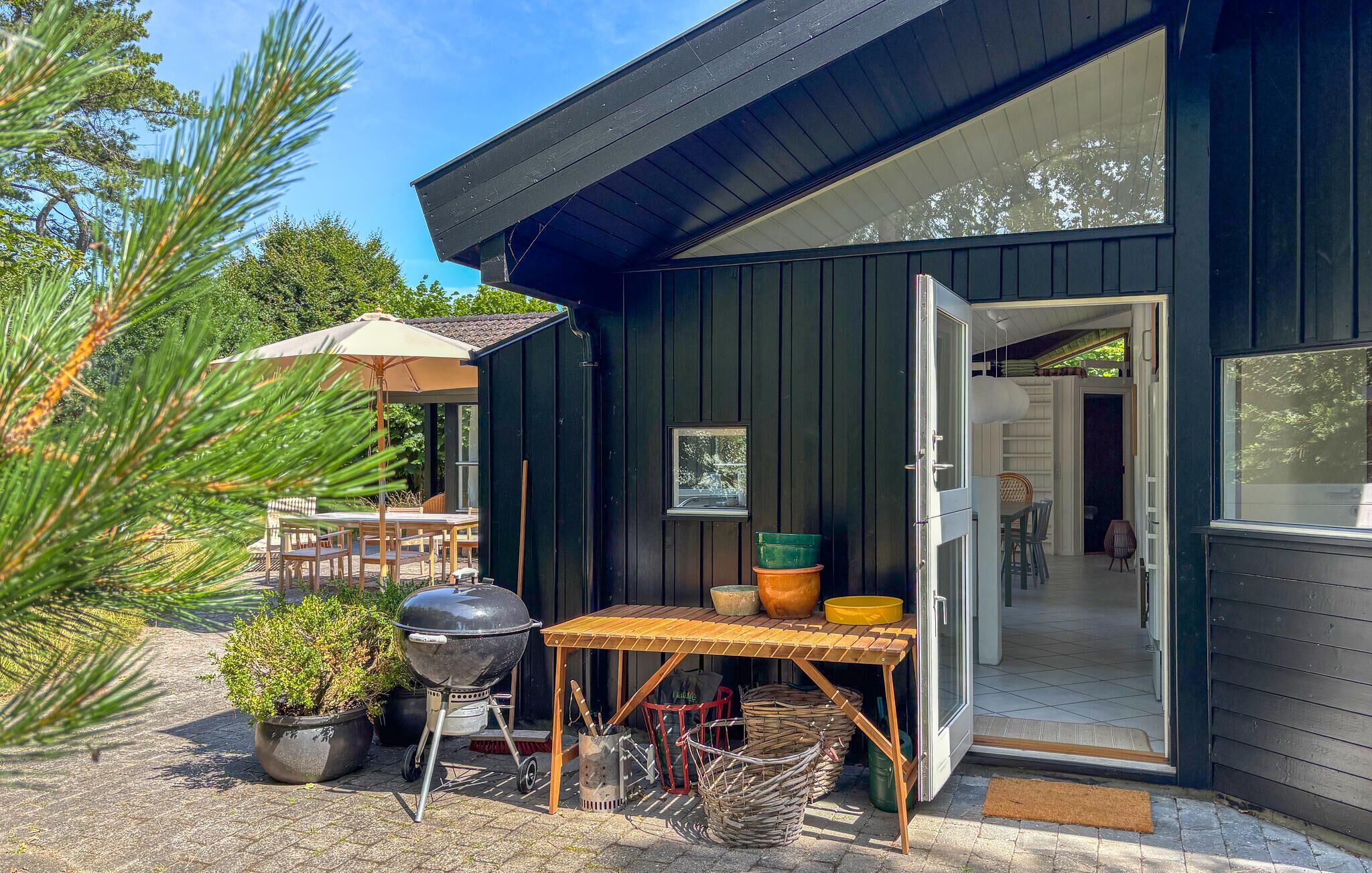 A wooden outdoor dining area with a grill, a table, and chairs.