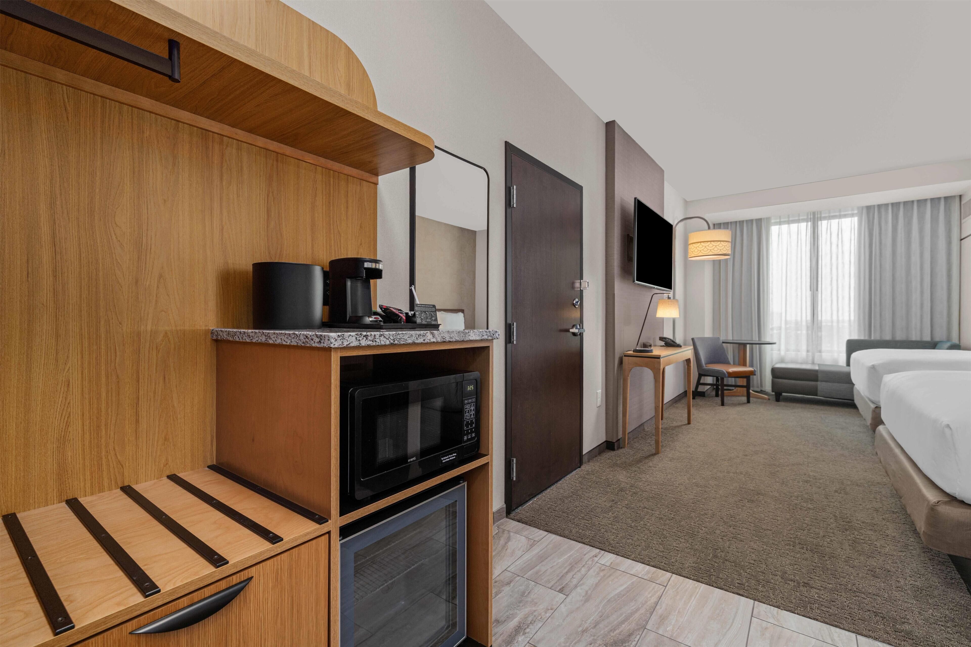 Une chambre d’hôtel équipée d’un lit, d’un bureau, d’un four à micro-ondes, d’une machine à café et d’une télévision.
