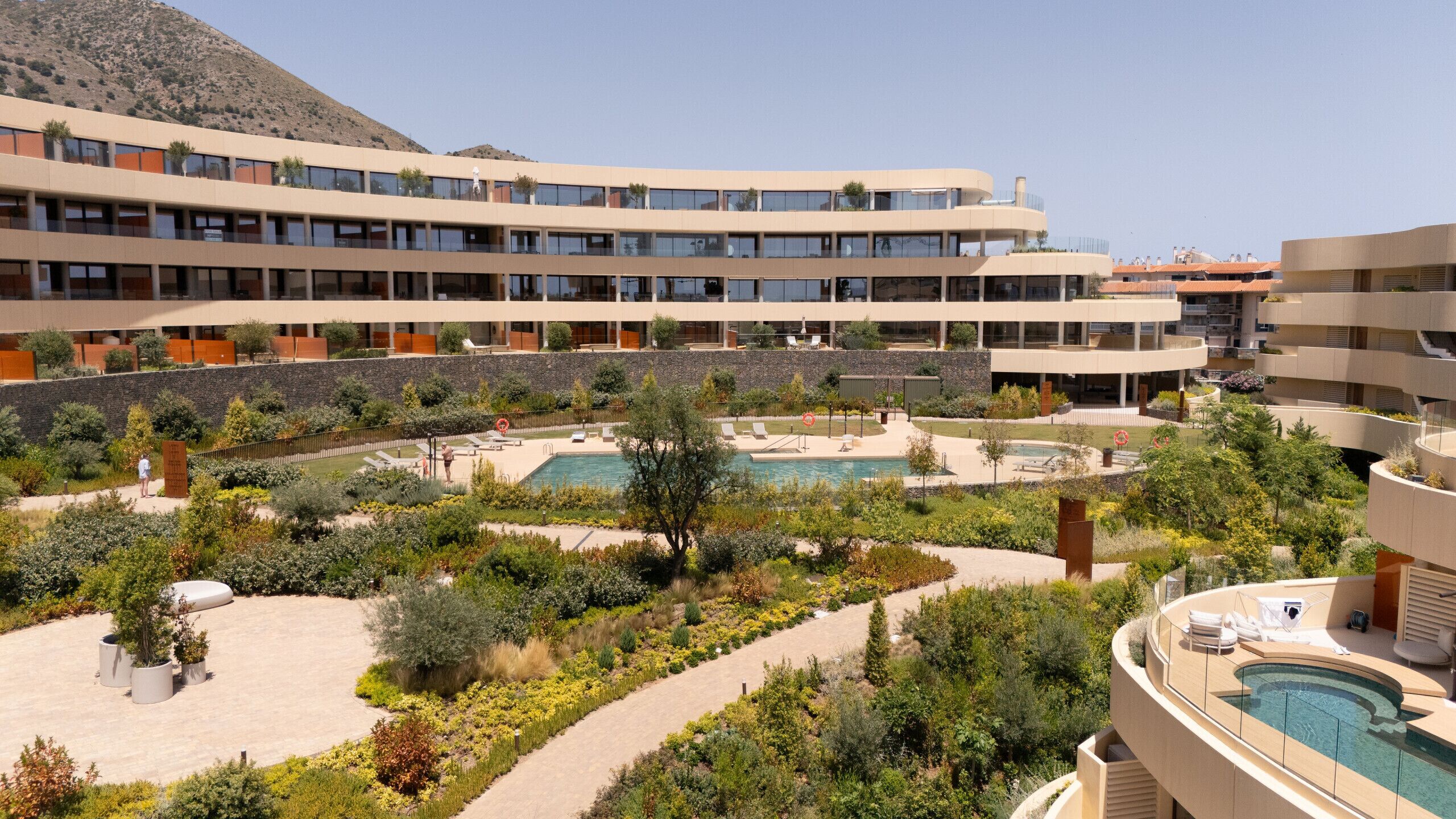 Un hotel con varias plantas, una piscina central y jardines ajardinados que lo rodean.