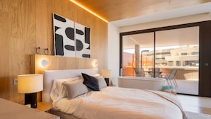 Ein modernes Schlafzimmer mit einem großen Bett, Nachttischlampen, einem Wandbild und einem Balkon mit Blick auf das Gebäude.
