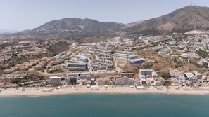 Eine Küstenlandschaft mit Strand, Wohnhäusern und Bergen im Hintergrund.