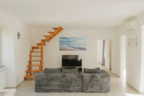 A living room with a wooden staircase, a flat-screen TV, and a large painting. - Tramonti Sunset Retreat | Jacuzzi, Panoramic Terrace & Amalfi Coast ⭐ (Campania)