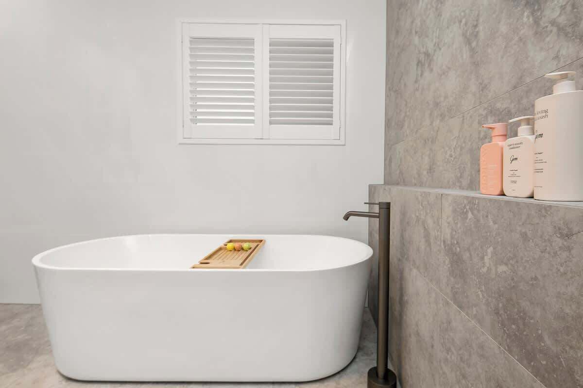 A modern bathroom with a freestanding bathtub, a wooden tray with fruits, and a shelf with toiletries.