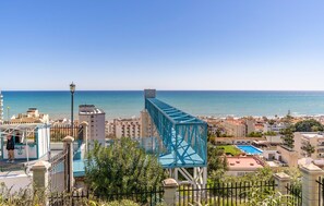 Eine Küstenstadtlandschaft mit einer markanten, blauen Brücke, Wohnhäusern und freiem Blick auf das Meer.