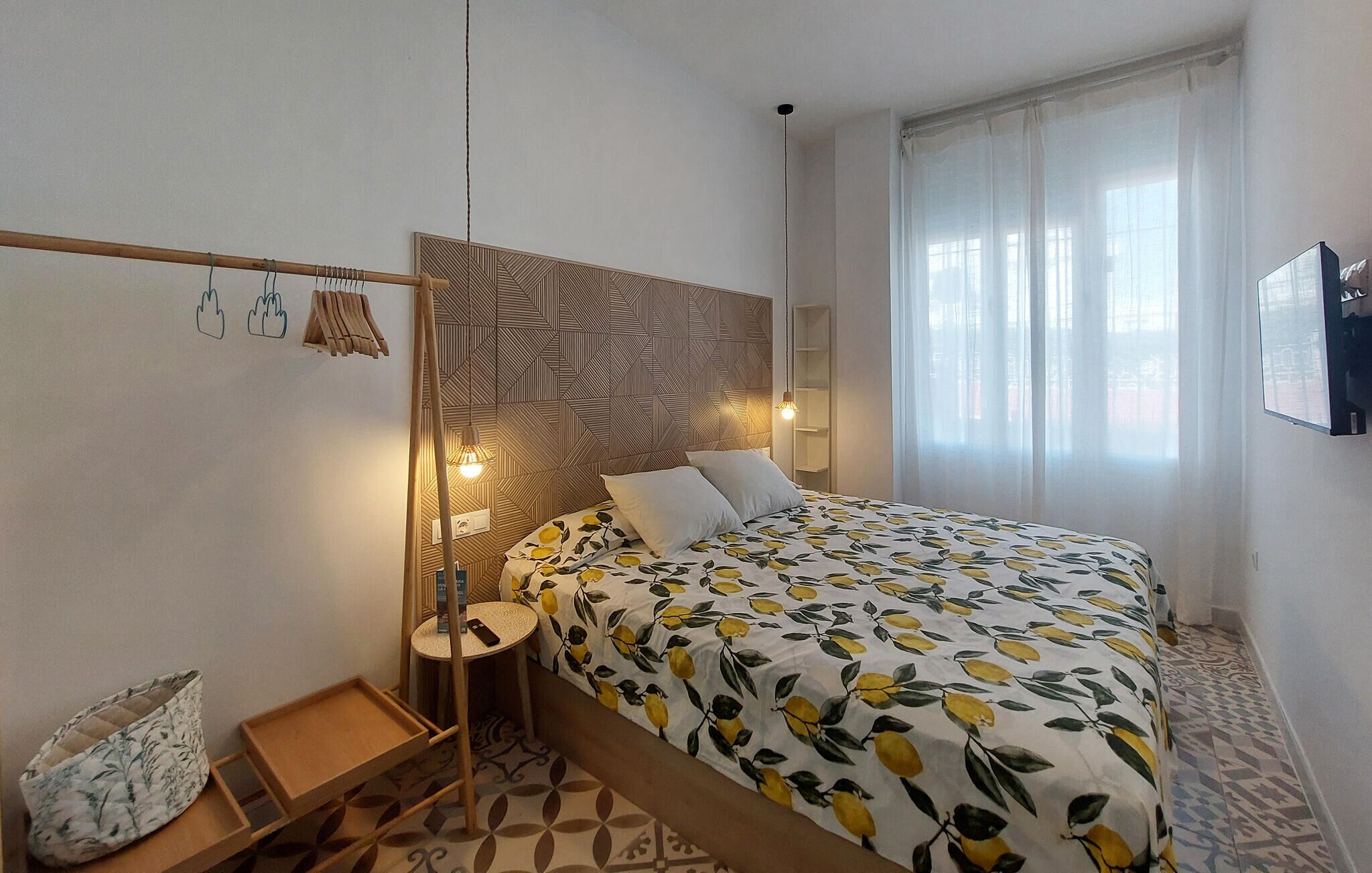 Une chambre à coucher avec une couvre-lit à motifs, une tête de lit au design géométrique, une table de chevet avec une lampe et une petite étagère.