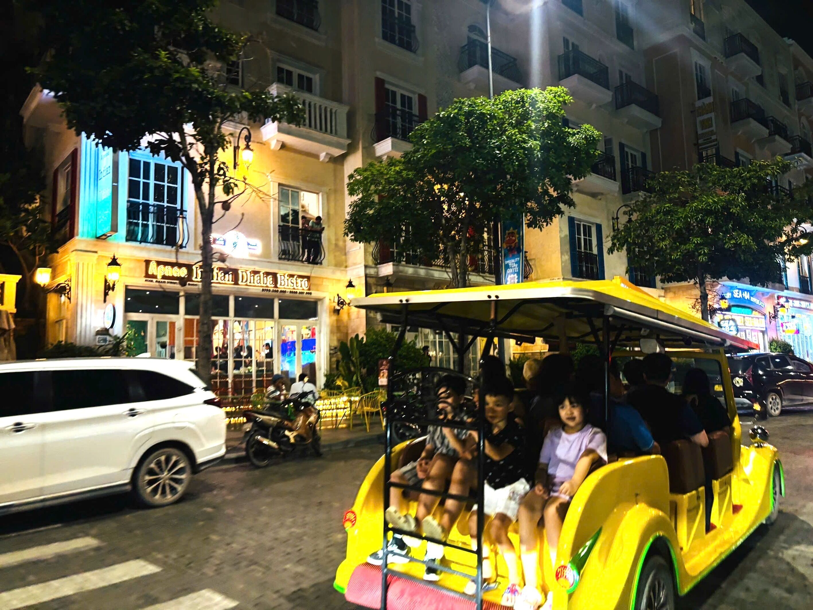 A yellow vehicle with passengers, parked in front of a building with a sign that reads 'Ameenah Dhaba Bistro.'