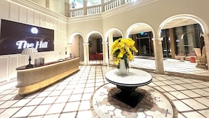 A lobby with a reception desk, a large screen displaying 'The Hill,' and a central area with a round table and yellow flowers.