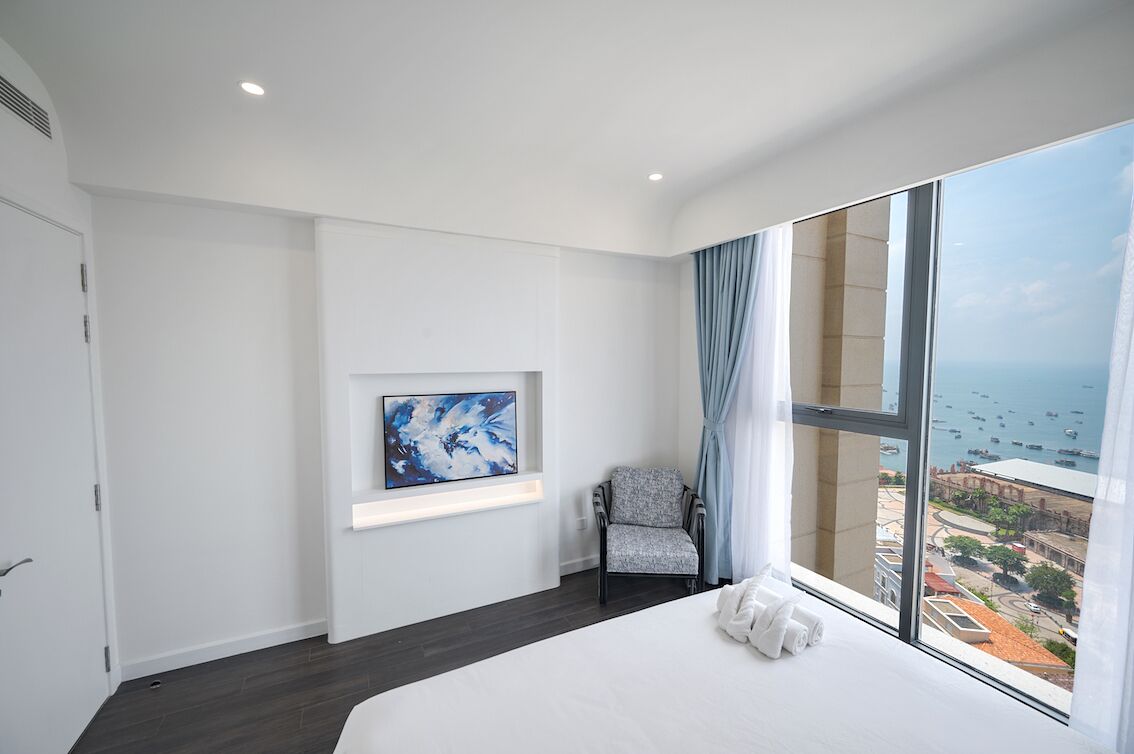 Une chambre d’hôtel moderne avec un grand lit, une chaise, un tableau et une vue sur la mer.
