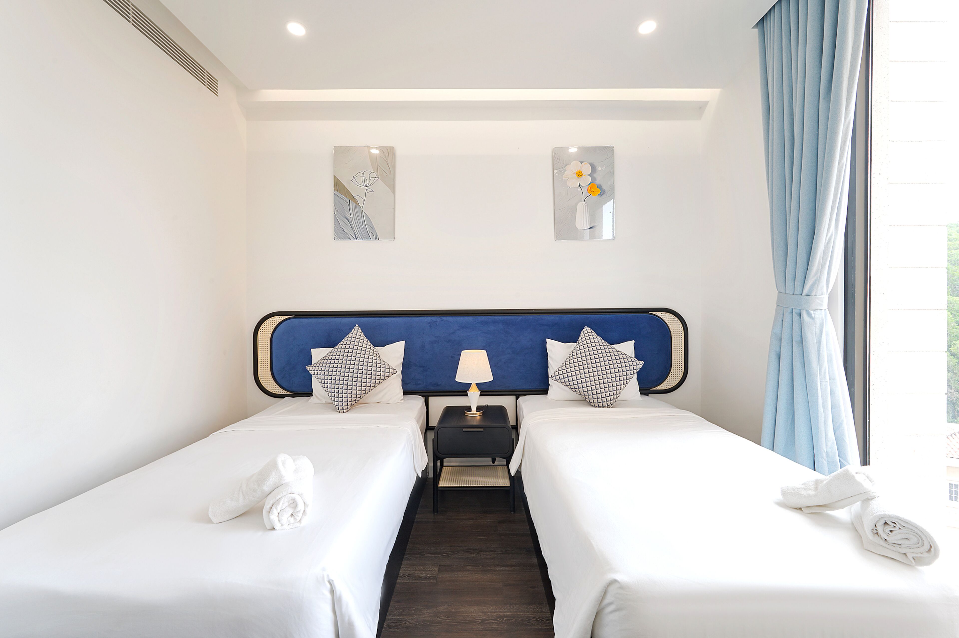 Habitación de hotel con dos camas, una mesita de noche, una lámpara y obras de arte en las paredes.