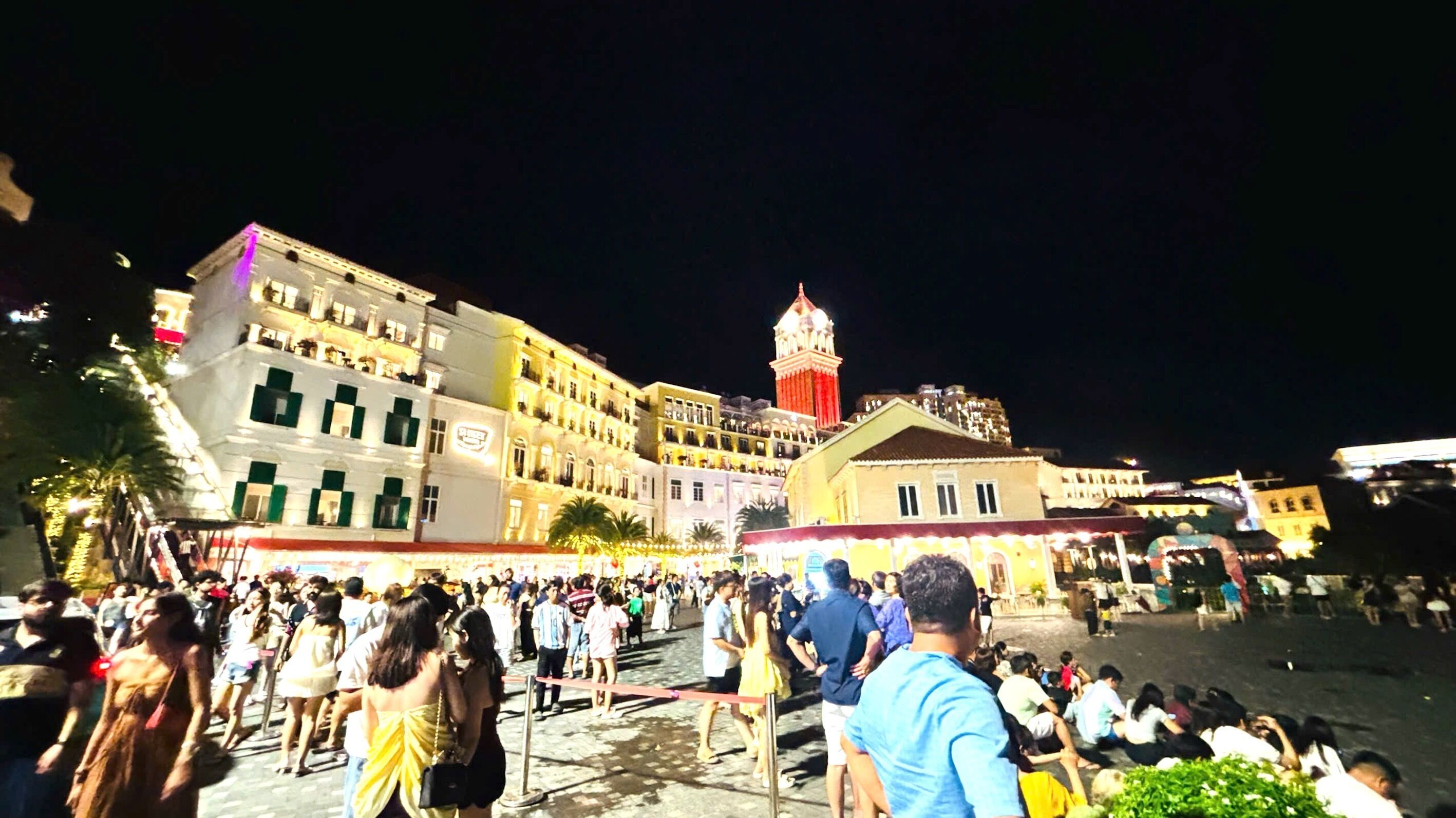 Uma praça movimentada com edifícios históricos e uma torre imponente.