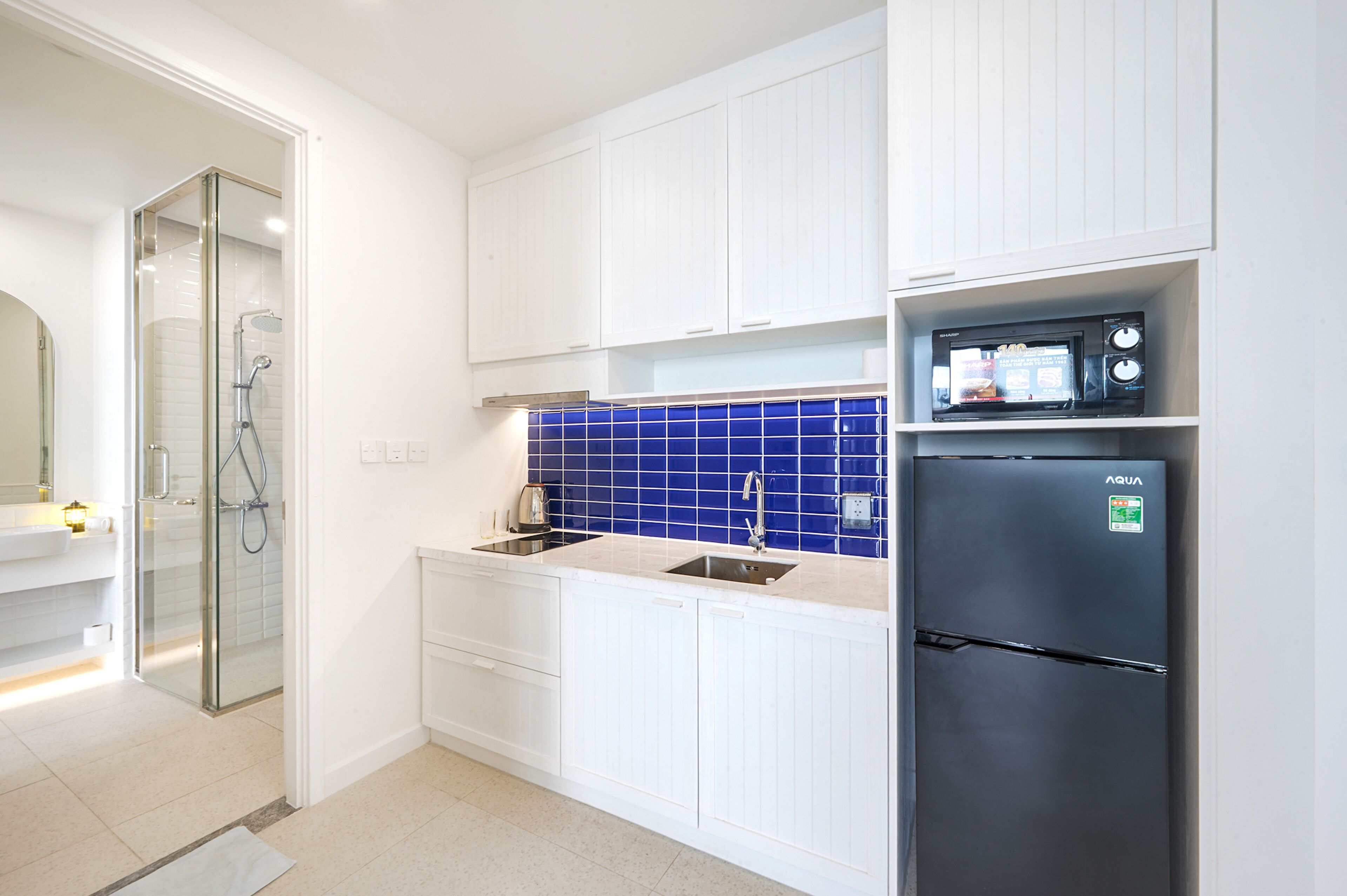 Eine moderne Küche mit weißen Schränken, einer blauen Fliesenspiegel und einem schwarzen Kühlschrank, sowie einer Duschkabine aus Glas.