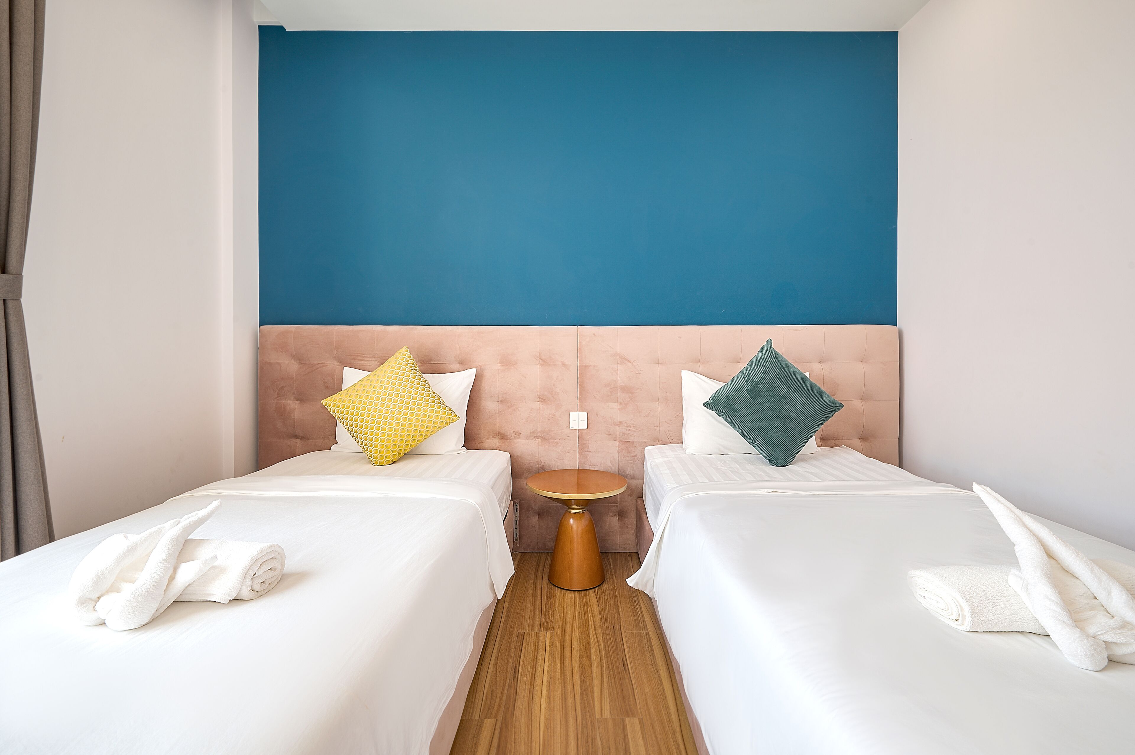 A hotel room with two beds, a round side table, and a blue accent wall.