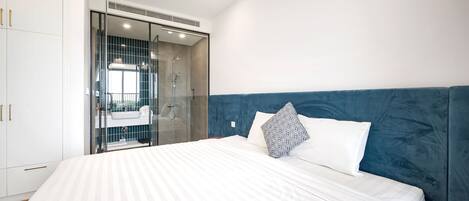 A modern bedroom with a large bed, a walk-in closet, and a glass shower enclosure.