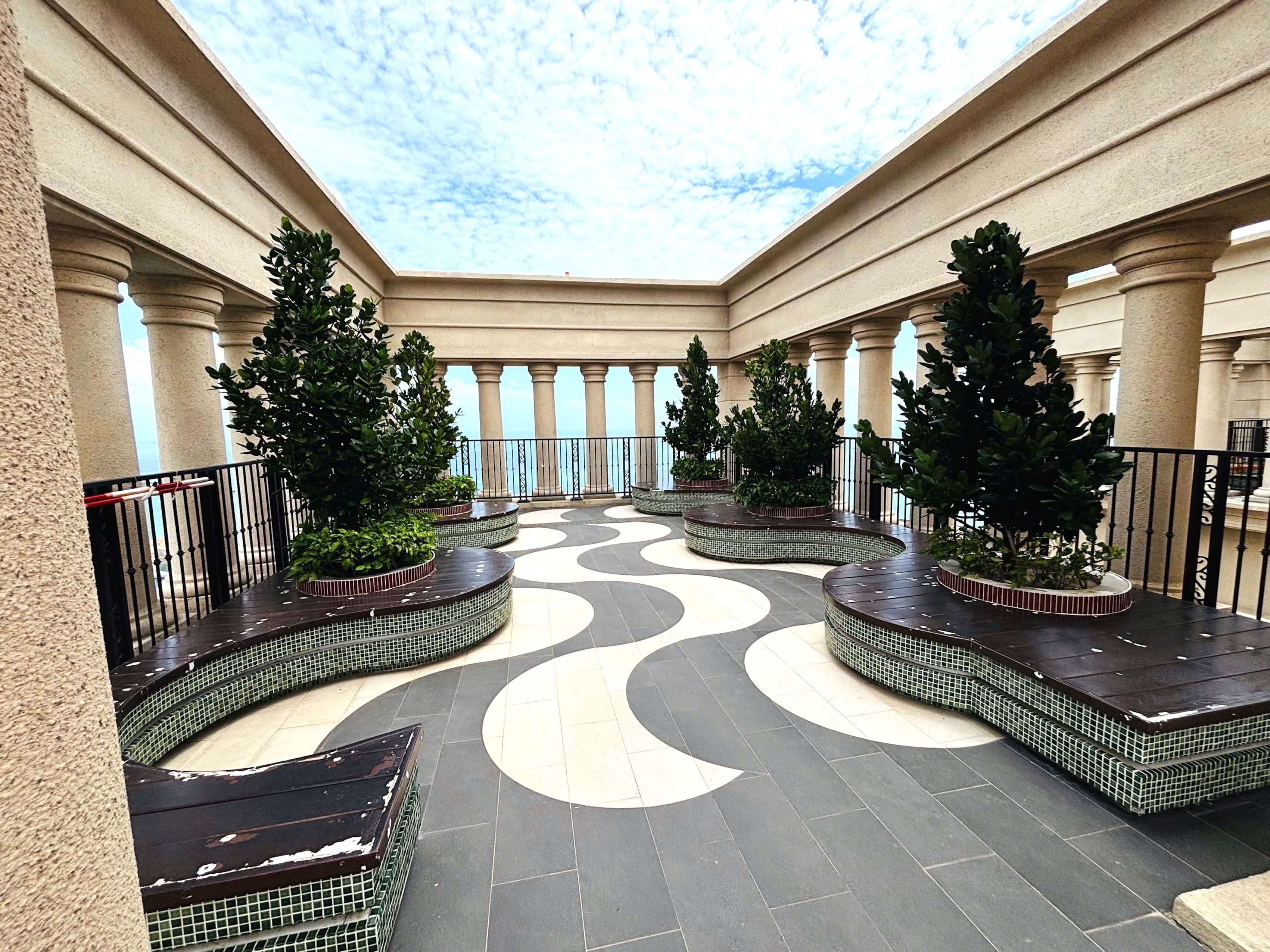 A covered outdoor area with a tiled floor, columns, and potted plants.