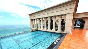 A rooftop swimming pool with a view of the ocean, surrounded by a balustrade and a tiled floor.