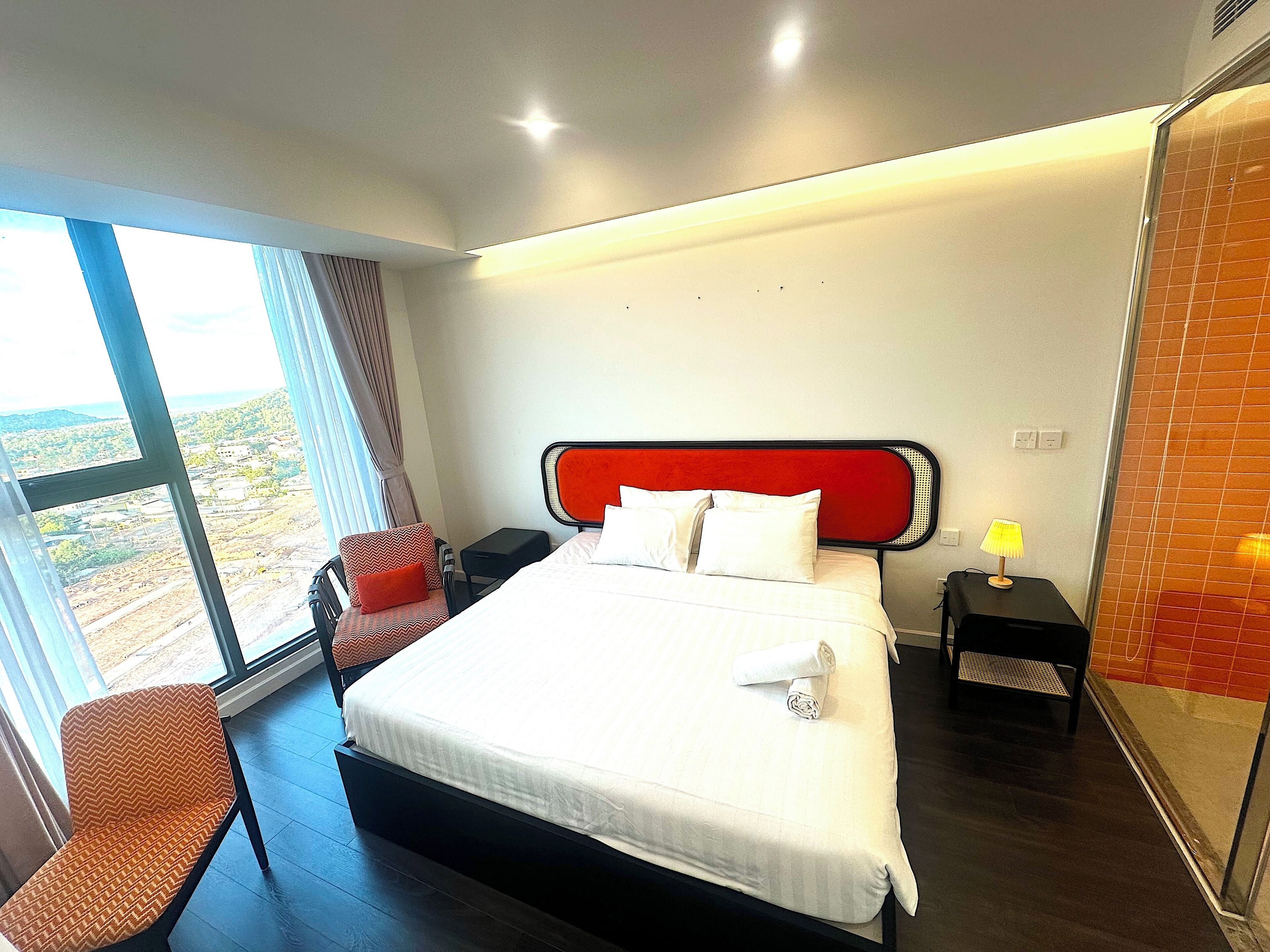 A hotel room with a bed, a chair, a nightstand, and a view of the outdoors.