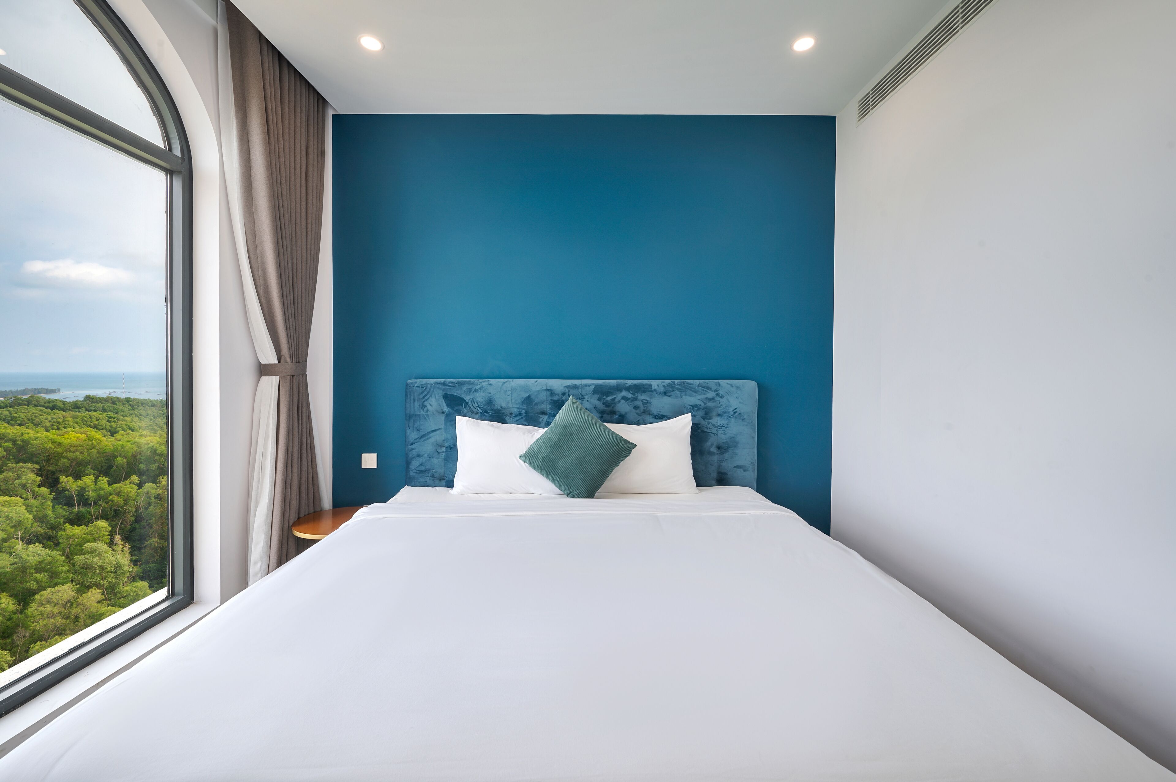 Un dormitorio con un ventanal grande, una cama con ropa de cama blanca y un almohada verde, y una pared de acento azul.