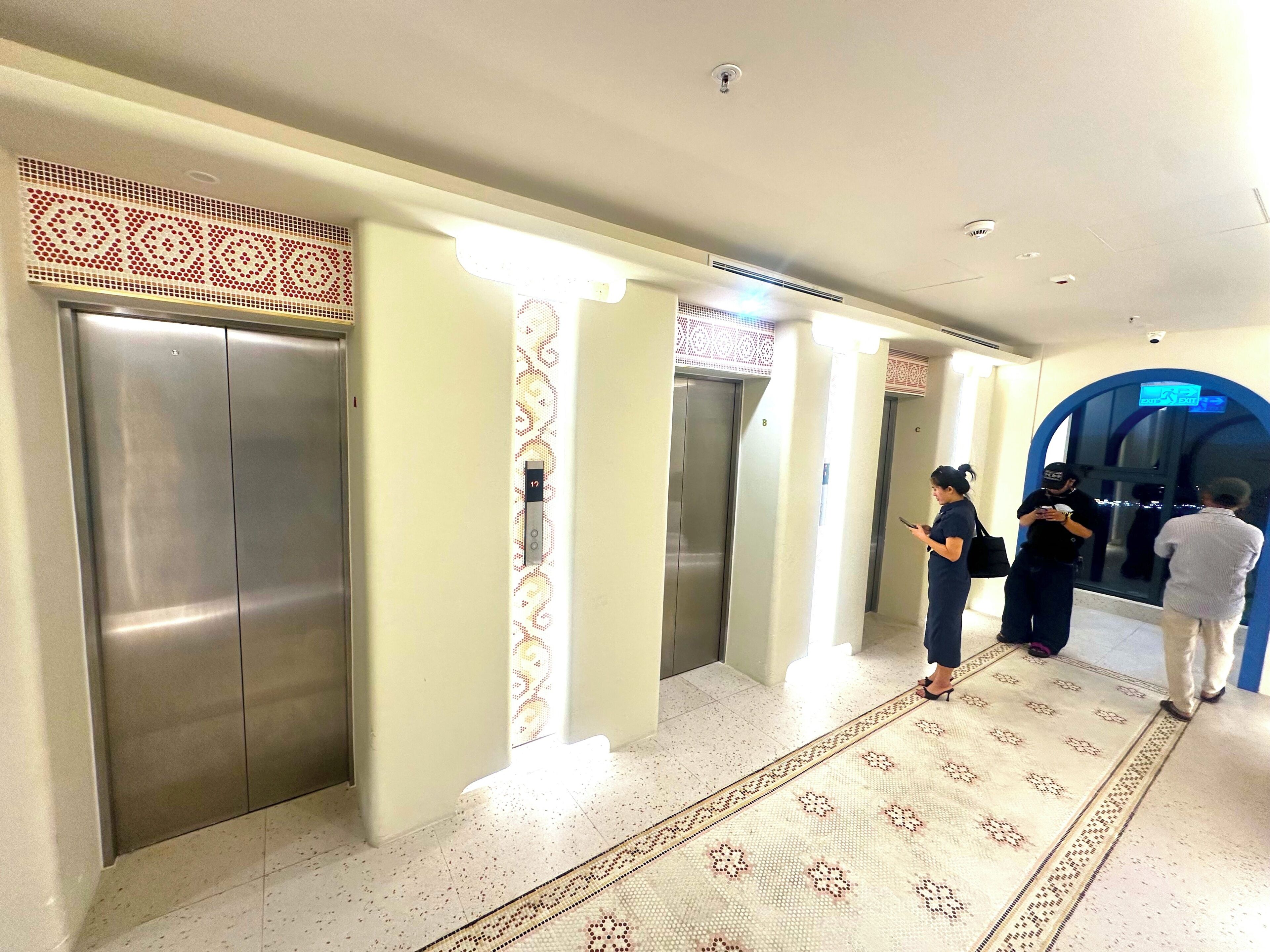 A hotel lobby with elevators, a patterned carpet, and a security guard.