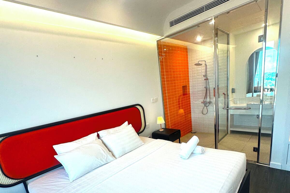 Habitación de hotel moderna con una cama grande, cabina de ducha de vidrio y vista al baño.