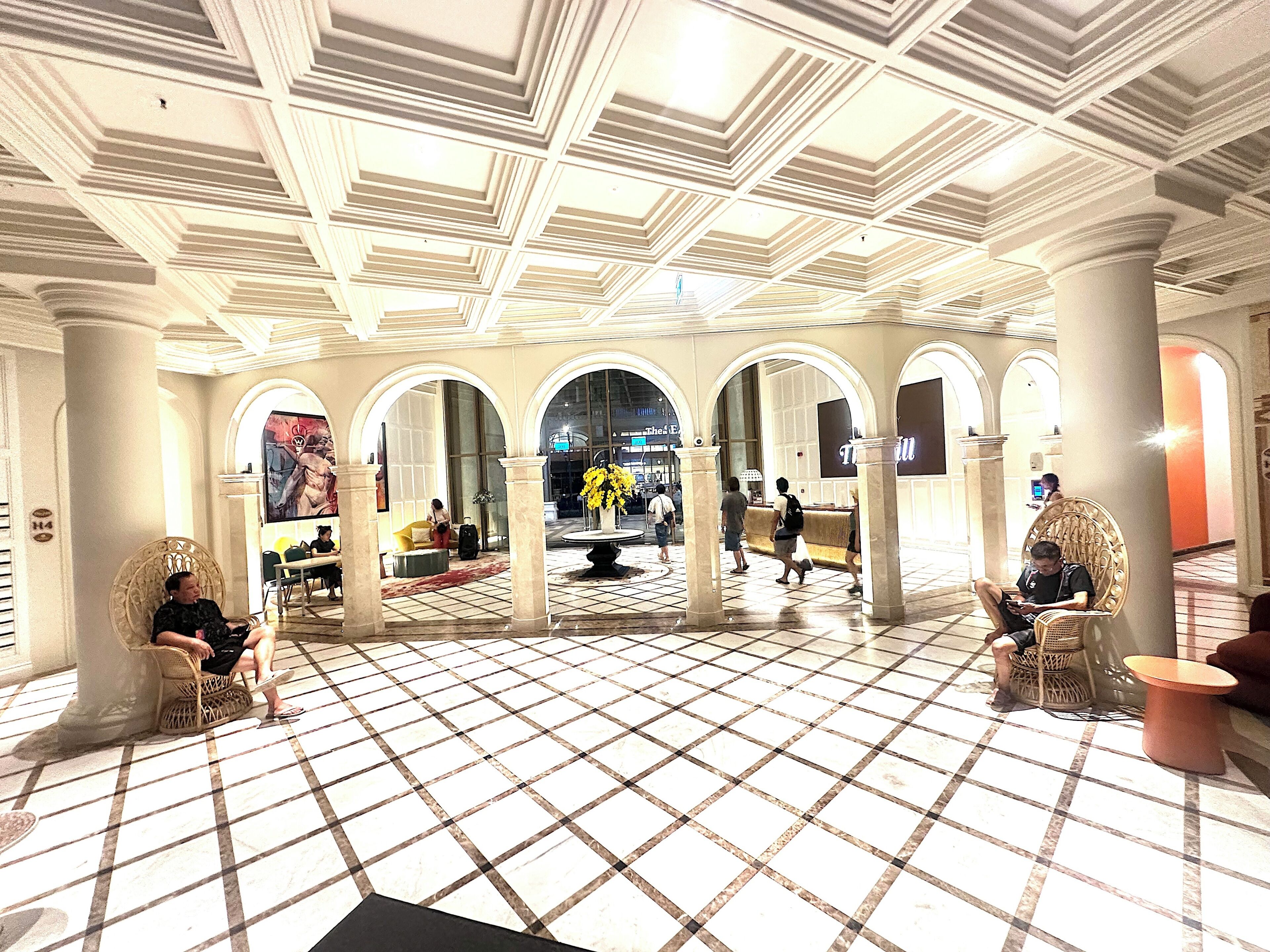 A lobby with a checkered floor, arched columns, and a central seating area with chairs and a table.