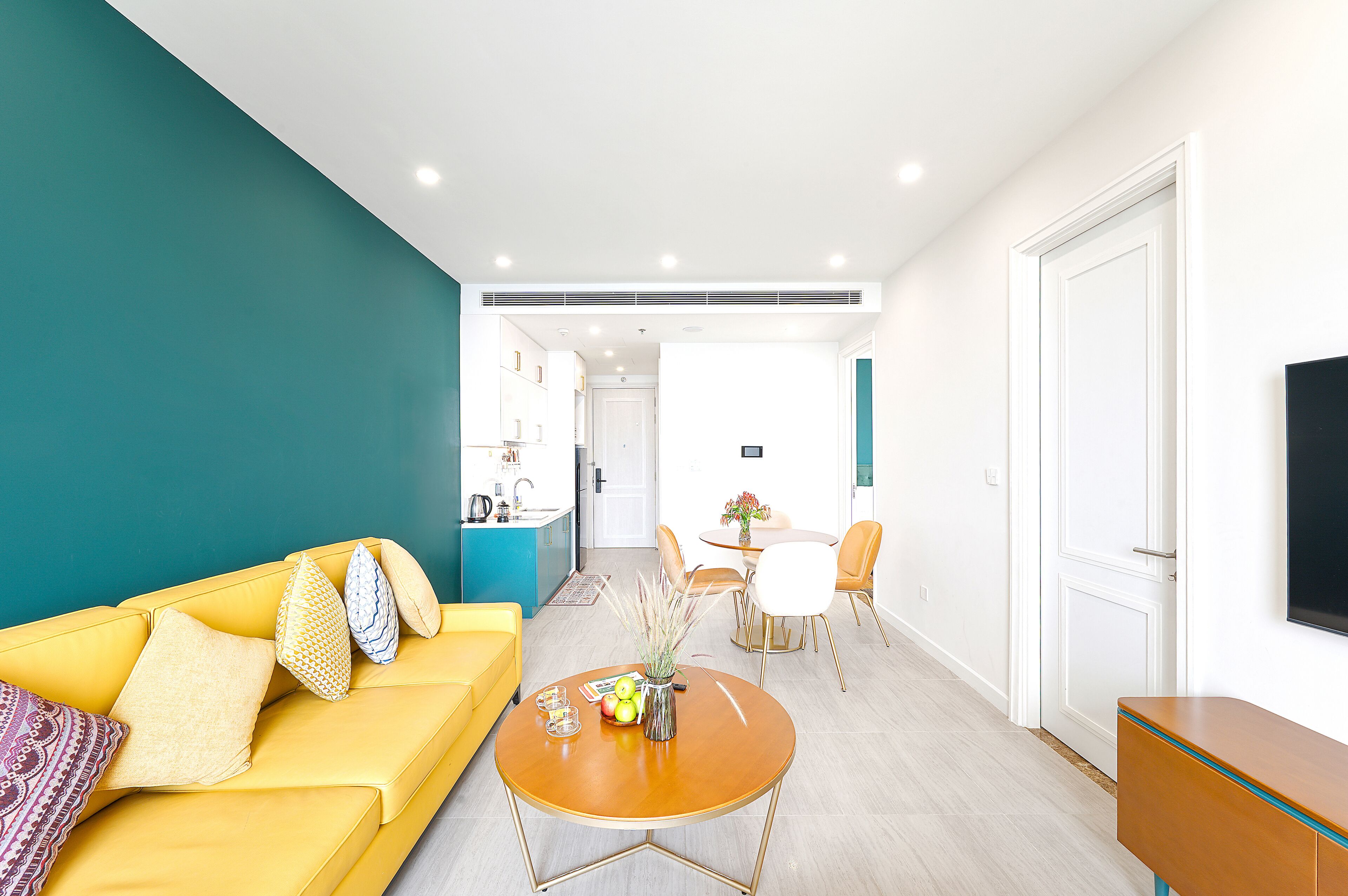 A modern living room with a yellow sofa, a round wooden coffee table, and a dining area with a white table and chairs.