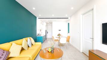 A modern living room with a yellow sofa, a round wooden coffee table, and a dining area with a white table and chairs.