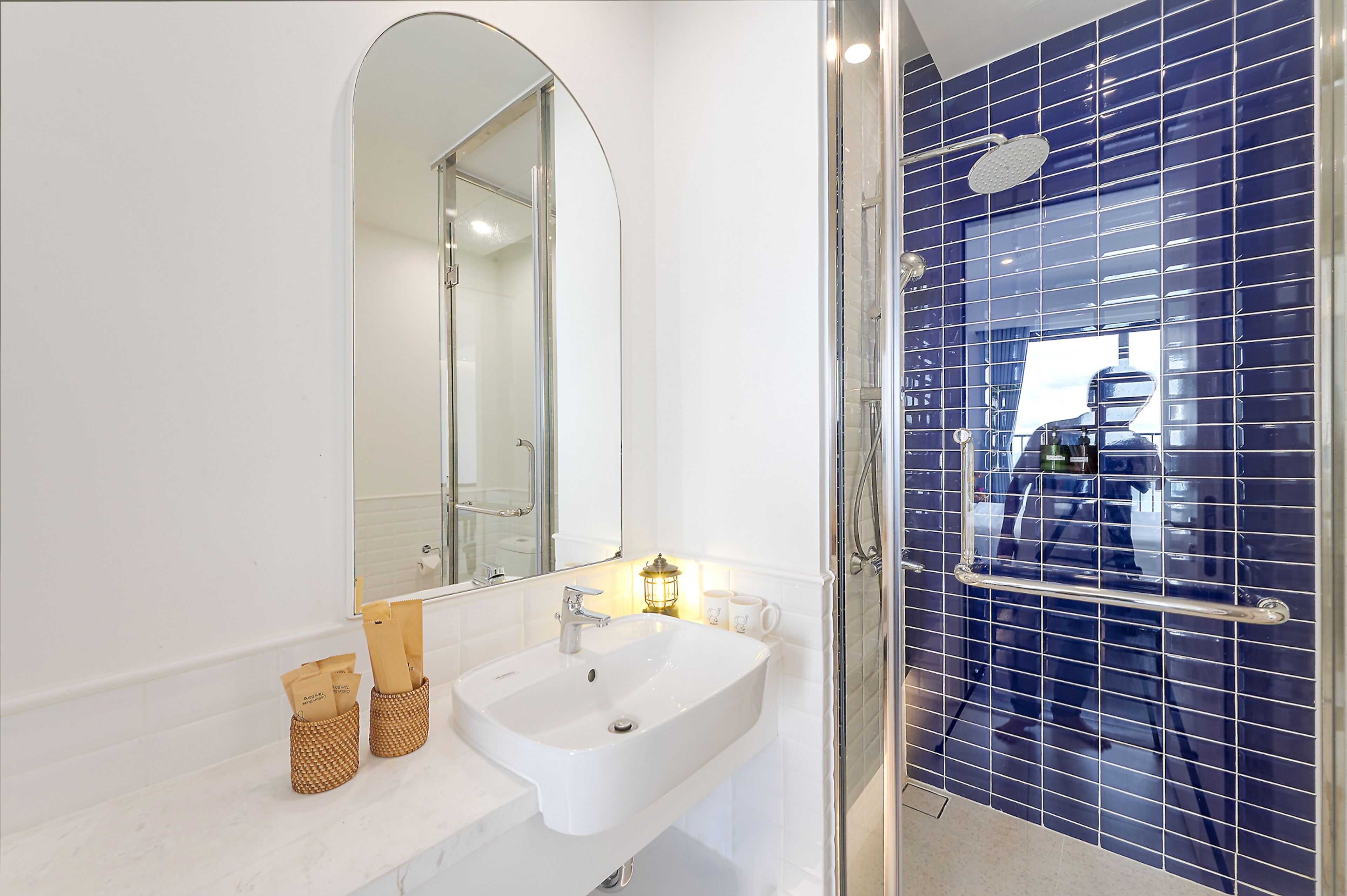 A bathroom with a white sink, a mirror, a shower with a glass door, and a blue tiled wall.