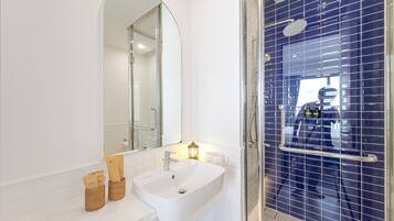 A bathroom with a white sink, a mirror, a shower with a glass door, and a blue tiled wall.