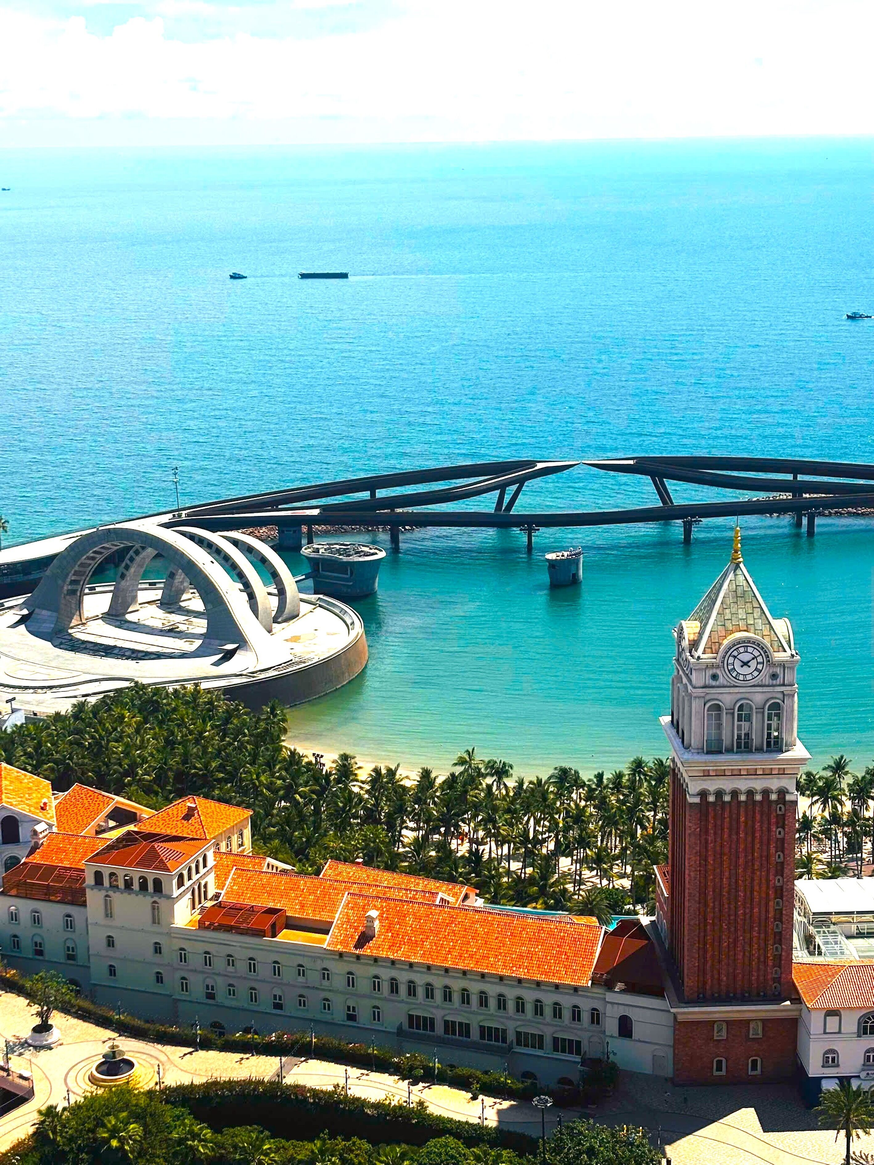 Paesaggio costiero con una torre dell'orologio imponente, un ponte e una struttura circolare con una cupola.
