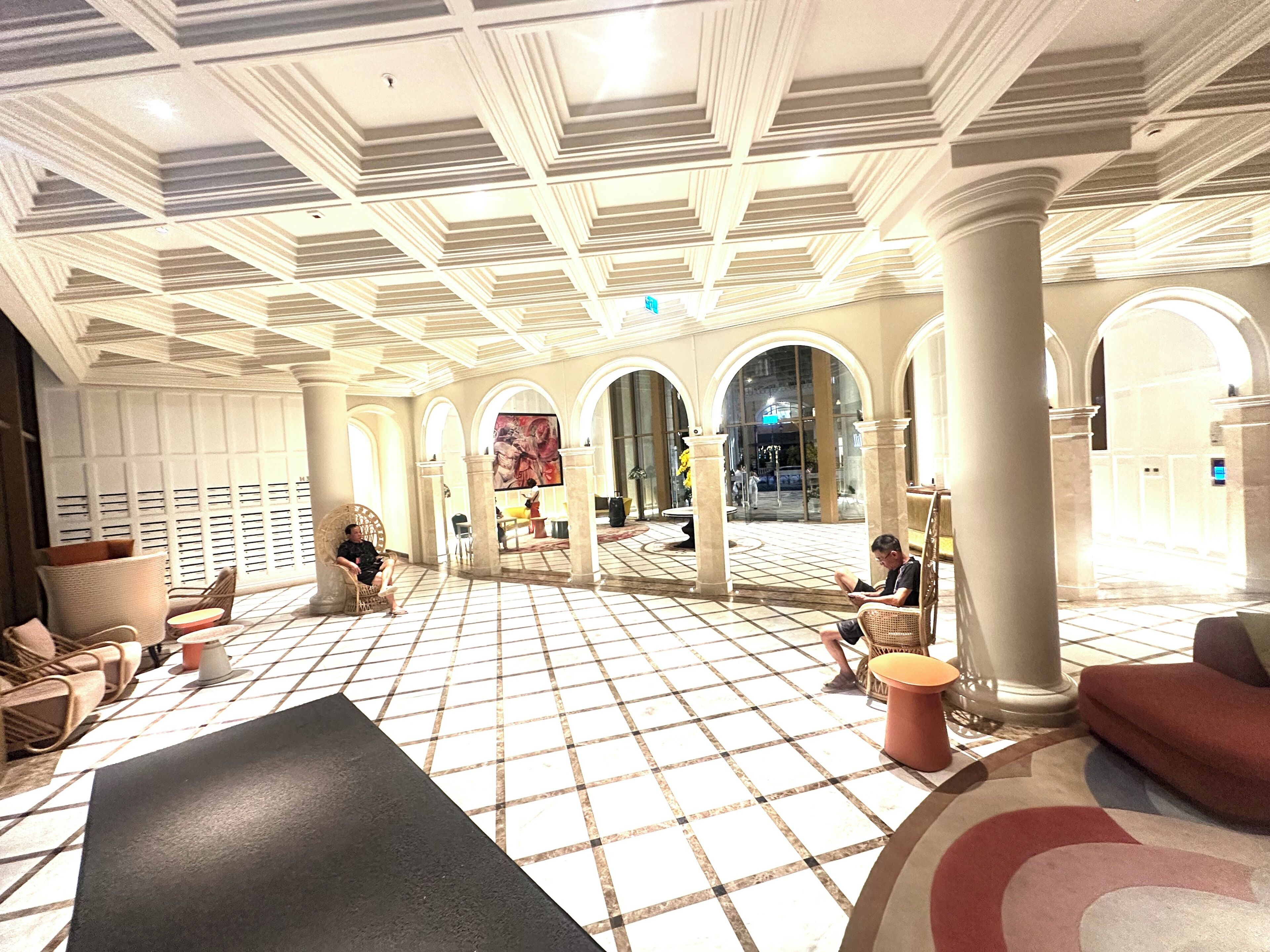 A spacious lobby with a checkered floor, arched columns, and a large painting on the wall.
