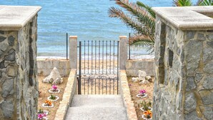 Un sentier de pierres menant à une porte donnant sur la plage, d’où l’on a une vue sur la mer.